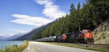 Train passes a lake in a valley. Trees in background. 